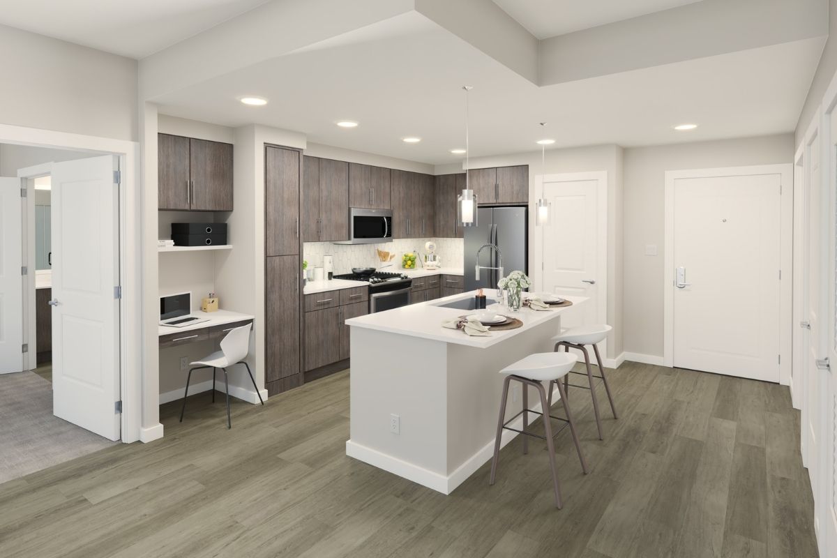 An apartment kitchen with wooden laminated floors, a bar with high chairs, and modern steel appliances.