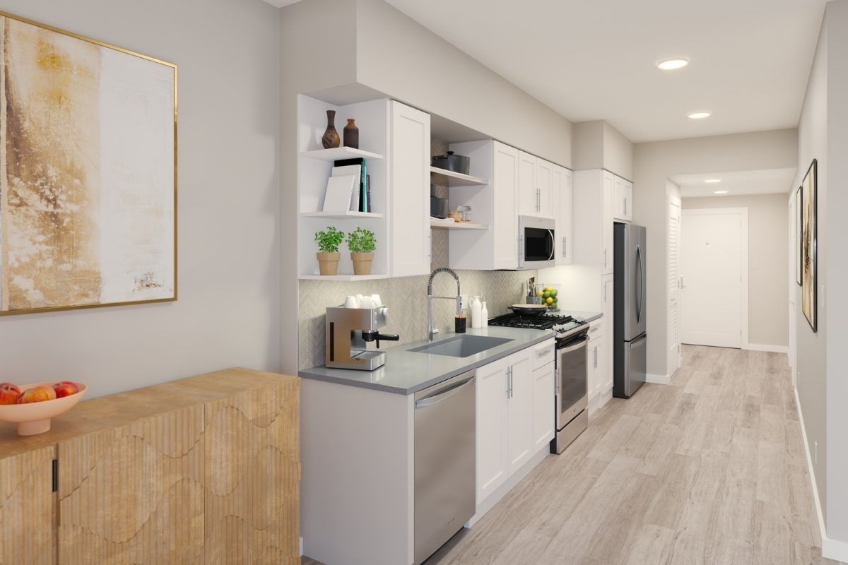 Hall view of a modern apartment kitchen featuring white cabinets and stylish steel appliances.