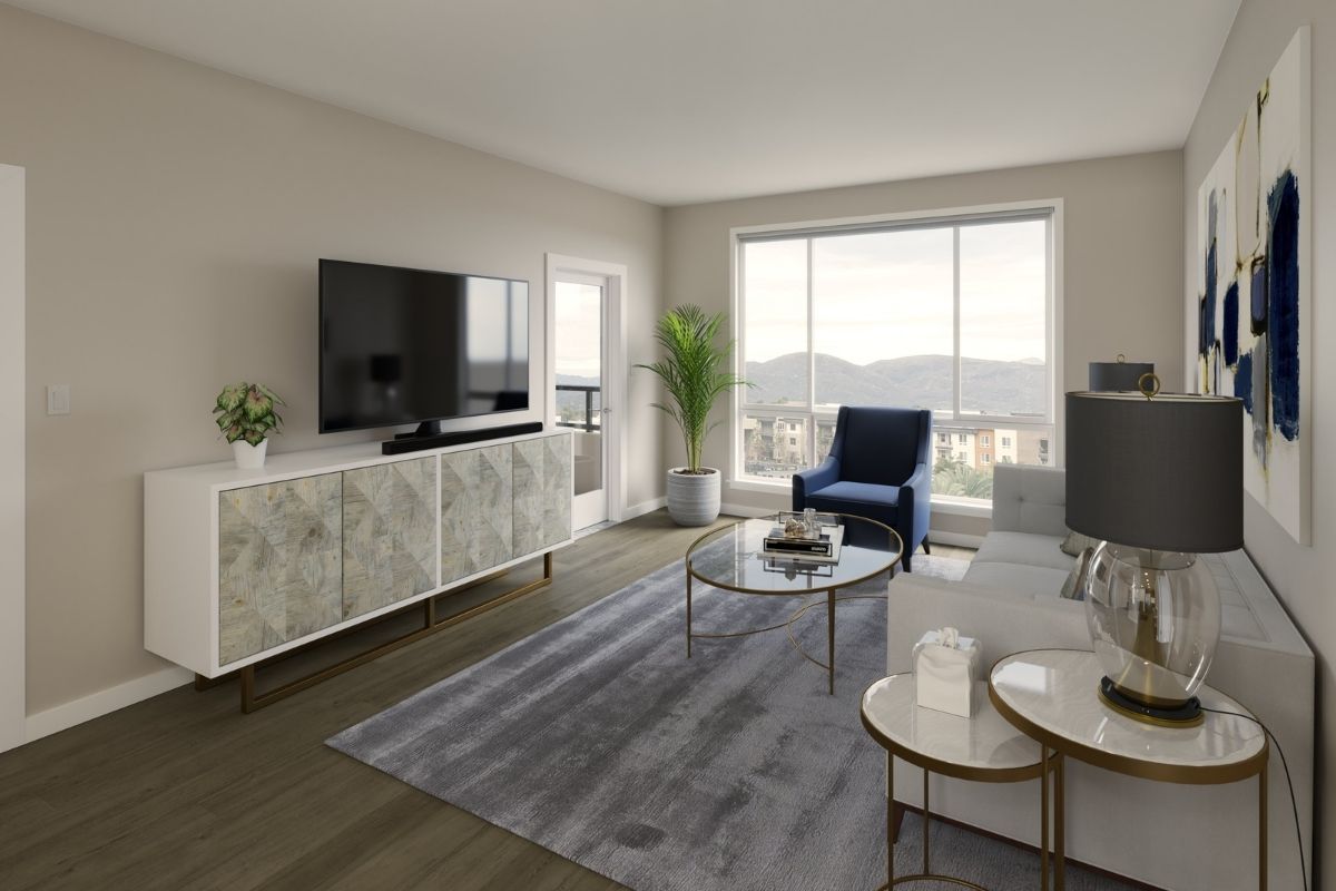 The living room area of a modern Chula Vista apartment featuring a carpet, stylish couch facing a tv above a wood furniture, and a window with a view.